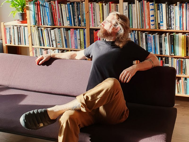 A picture of Sjef van Gaalen sitting on the couch in front of full bookshelves